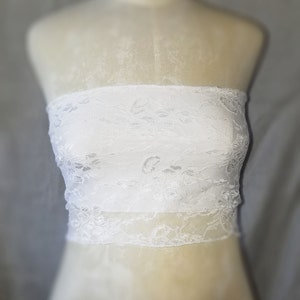 May include: White lace bandeau top with a delicate floral pattern.