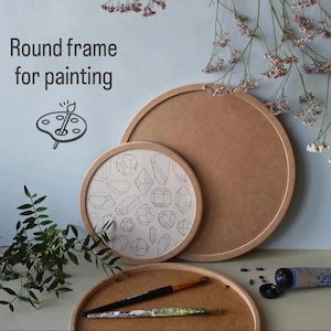 Puede incluir: Tres marcos redondos de madera para pintar, el más grande está vacío, el marco del medio presenta un patrón de formas geométricas y el marco más pequeño con dos pinceles en la parte superior. El texto "Round frame for painting" es visible en la parte superior de la imagen.