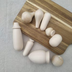 Könnte beinhalten: Ein Set aus neun unfertigen Holzpuppen-Teilen, bestehend aus Kopf, Rumpf, Armen und Beinen. Die Teile sind alle glatt und unbemalt, bereit zum Basteln.