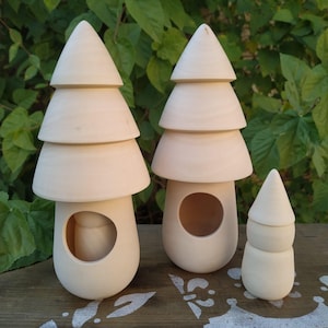 Puede incluir: Tres esculturas de madera sin terminar con forma de hongo. Dos hongos más grandes tienen una base redondeada con una abertura circular y una parte superior cónica escalonada. Un hongo más pequeño tiene un diseño similar. Las esculturas son de color beige claro.