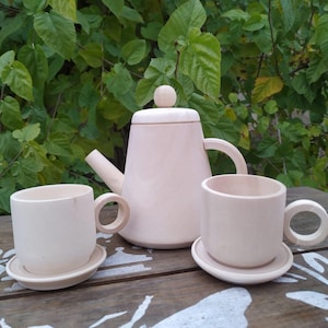 May include: A wooden tea set featuring a teapot, two cups, and two saucers. The set is crafted from natural wood and has a light brown colour.