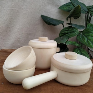 Könnte beinhalten: Ein Set aus Holzspielzeug-Küchenutensilien, bestehend aus zwei Töpfen mit Deckeln und zwei Schüsseln. Die Töpfe und Schüsseln sind aus Naturholz gefertigt und haben eine glatte, unbehandelte Oberfläche.