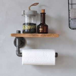 May include: A rustic wooden shelf with black metal pipe supports and a paper towel holder. The shelf is holding a glass jar with black and green beans, a small brown glass bottle labeled "OIL", and a gray concrete lid.