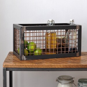May include: A black metal wire storage basket with a copper finish. The basket is filled with limes and glass bottles. The basket is sitting on a wooden table.