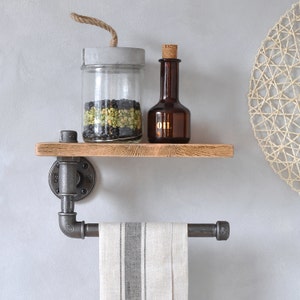 May include: A rustic wooden shelf with black metal pipe supports and a towel rack. The shelf is holding a glass jar filled with black and green peppercorns and a small brown glass bottle labeled "OIL".