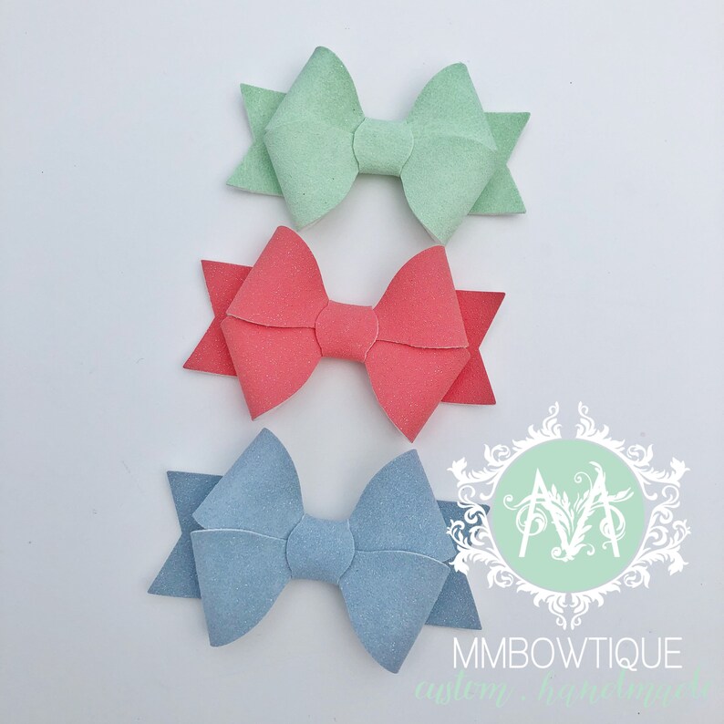 May include: Three felt hair bows in different colors: light blue, coral, and light green. The bows are arranged in a vertical stack, with the light blue bow at the bottom, the coral bow in the middle, and the light green bow at the top.