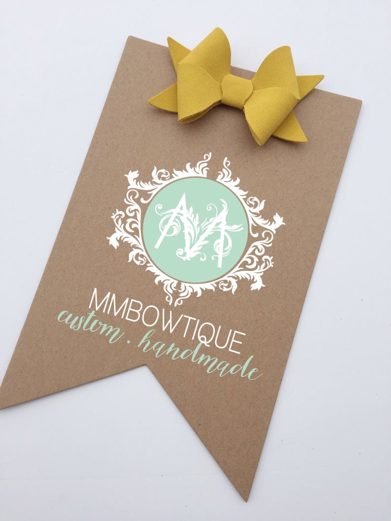 May include: A brown paper tag with a white logo featuring a stylized "MM" in a circle with a green background and a white floral design. The text "MMBOWTIQUE custom. handmade" is printed below the logo.