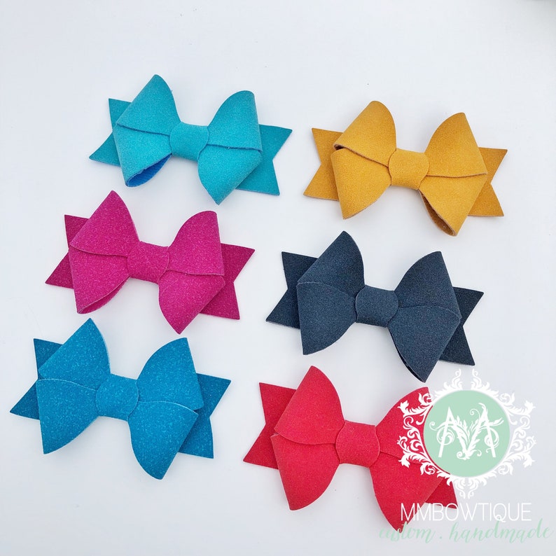 May include: Six felt hair bows in various colors, including teal, mustard yellow, pink, dark blue, turquoise, and red. The bows are arranged in two rows of three.
