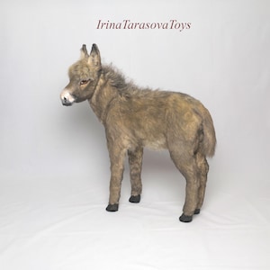 May include: A lifelike, plush donkey toy in shades of brown and tan, standing on a white surface. The toy has detailed features, including a light-colored muzzle and dark hooves. The text "Irina Tarasova Toys" is in the upper right corner.