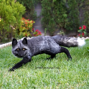 May include: A silver fox plush toy with black legs and a white tipped tail. The fox is standing on green grass.
