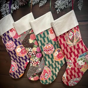 May include: Four Christmas stockings with white cuffs and colorful patterned designs. The stockings feature various patterns, including geometric shapes, floral motifs, and decorative ball designs. The color palette includes purple, brown, green, and red.