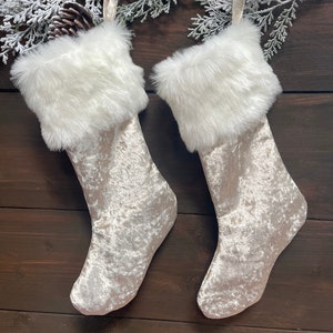 May include: Two white faux fur-trimmed Christmas stockings with a shimmery silver velvet fabric.