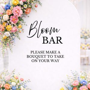 May include: A white Bloom Bar sign with floral arrangements. The sign has the words "Bloom BAR" in black script. The sign also says "PLEASE MAKE A BOUQUET TO TAKE ON YOUR WAY". Colorful flowers in pink, yellow, and blue surround the sign.