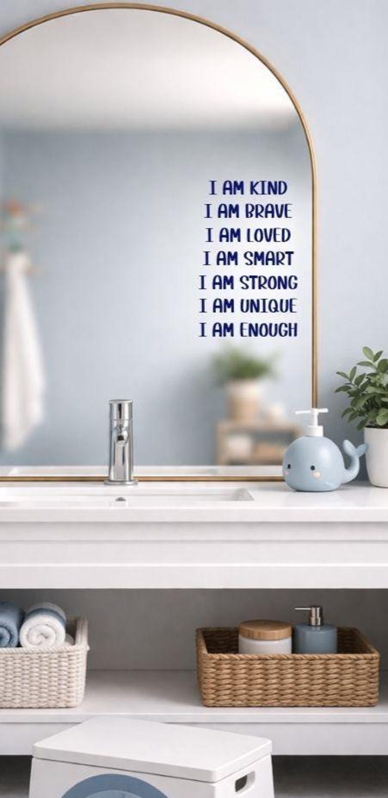 Puede incluir: Interior de ba&ntilde;o con un espejo con marco dorado que muestra el texto "I AM KIND, I AM BRAVE, I AM LOVED, I AM SMART, I AM STRONG, I AM UNIQUE, I AM ENOUGH" en azul. Un dispensador de jab&oacute;n azul con forma de ballena est&aacute; sobre la encimera blanca.
