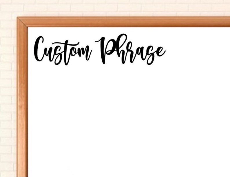 May include: A rectangular white board with a thin wooden frame. The words Custom Phrase are written in black cursive script across the upper portion of the white surface. The board has a clean, flat design with a smooth, bright white center area.