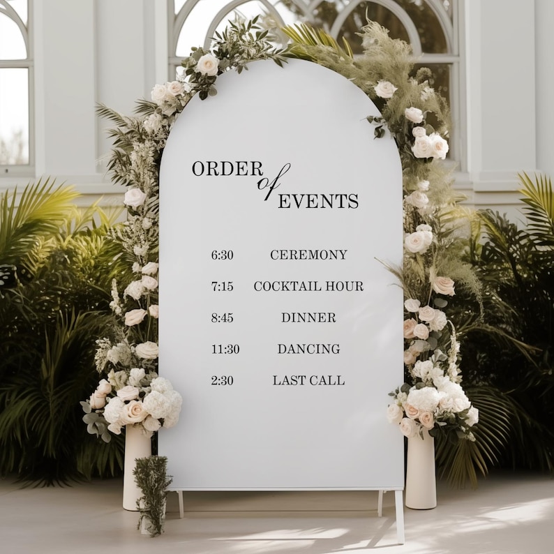 Pode incluir: Uma placa arqueada branca exibindo o texto ORDER OF EVENTS com um cronograma incluindo 6:30 CEREMONY, 7:15 COCKTAIL HOUR, 8:45 DINNER, 11:30 DANCING e 2:30 LAST CALL, emoldurada por folhas de palmeira verdes e arranjos florais brancos.