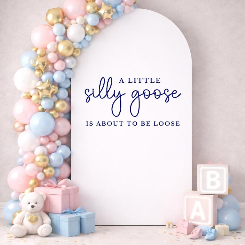 Op de afbeelding: Een witte boog met de tekst "A little silly goose is about to be loose" is omgeven door een ballonnenboog in roze, blauw en goud. Een teddybeer, cadeau dozen en babyblokken maken het babyshower thema compleet.