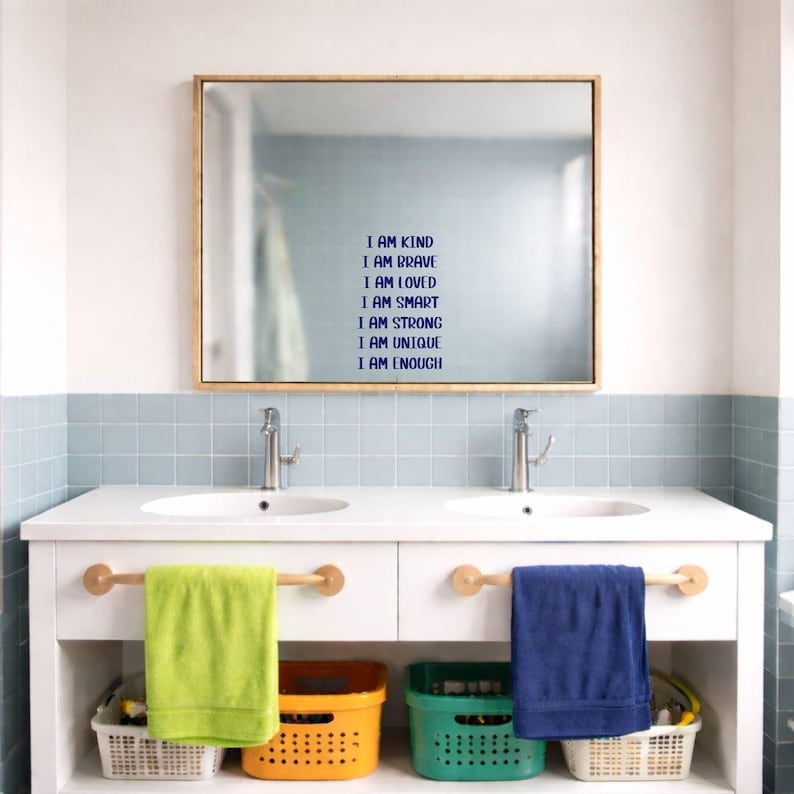 Puede incluir: Un mueble de ba&ntilde;o con un espejo grande y dos lavabos. El espejo tiene un marco de madera y el texto "I AM KIND, I AM BRAVE, I AM LOVED, I AM SMART, I AM STRONG, I AM UNIQUE, I AM ENOUGH." Debajo hay dos toallas, una verde y otra azul.