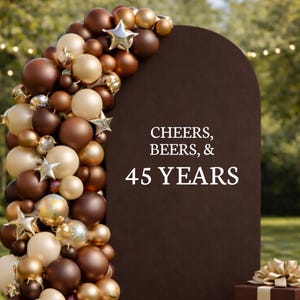 May include: A brown arch with the text "CHEERS, BEERS, & 45 YEARS" is decorated with gold, brown, and cream-colored balloons and star-shaped ornaments. A gift box with a gold bow is in the bottom right corner.