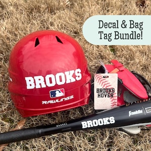 May include: A red Rawlings baseball helmet with the name BROOKS in white, a black baseball bat with the name BROOKS, and a rectangular bag tag featuring a baseball graphic and the text BROOKS HOVER. A light green sign reads Decal & Bag Tag Bundle!