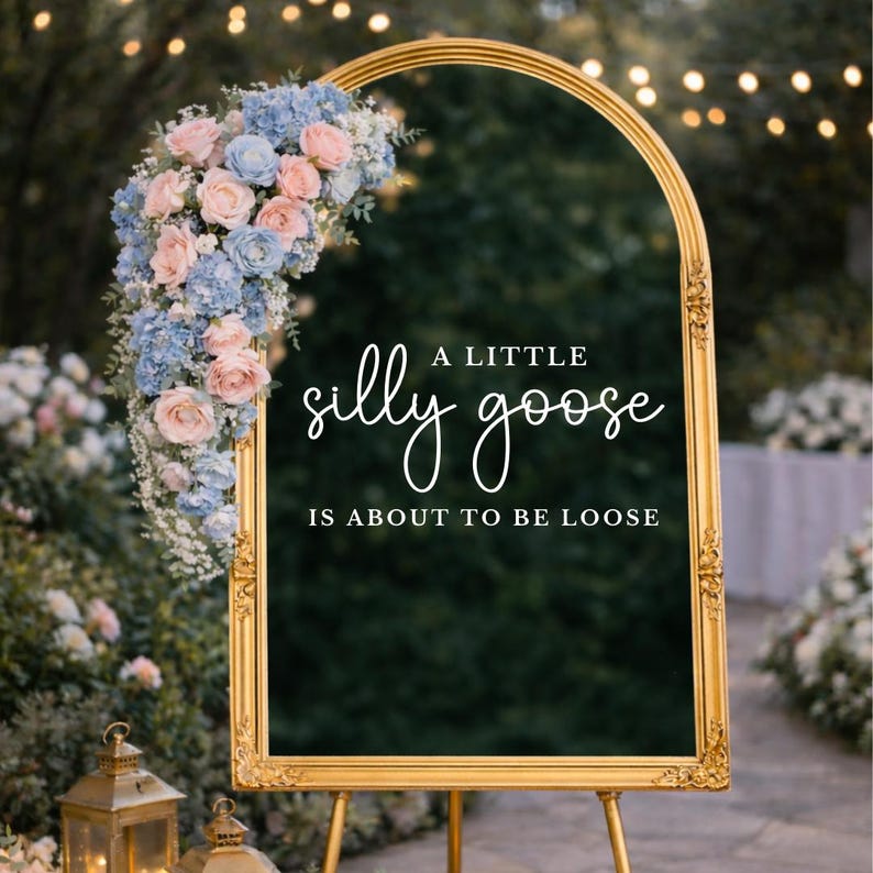 Op de afbeelding: Een goudkleurig bord met de tekst "A little silly goose is about to be loose". Het bord is versierd met roze en blauwe bloemen. Het bord staat op een gouden ezel.