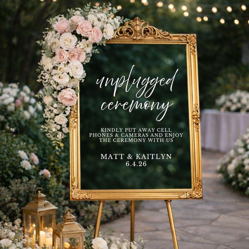 May include: A gold ornate frame holding a dark sign that reads unplugged ceremony, kindly put away cell phones & cameras and enjoy the ceremony with us, Matt & Kaitlyn, 6.4.26. A large arrangement of white and pink roses decorates the top left corner.