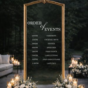 Pode incluir: Um espelho retangular alto com uma moldura dourada ornamentada, apresentando texto em branco que diz ORDER of EVENTS seguido por um cronograma das 16:00 CEREMONY &agrave;s 23:30 LAST CALL. O espelho &eacute; decorado com arranjos florais brancos na base.