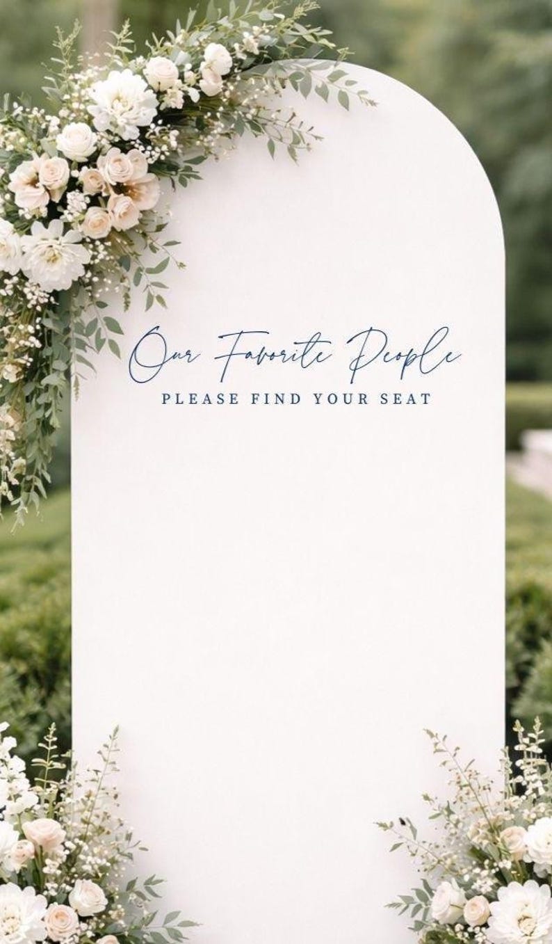 Op de afbeelding: Een wit boogvormig bord met de tekst "Our Favorite People" in een donkerblauw handschrift en "PLEASE FIND YOUR SEAT" in een donkerblauw schreeflettertype. Het bord is versierd met witte bloemen en groen blad aan de hoeken.