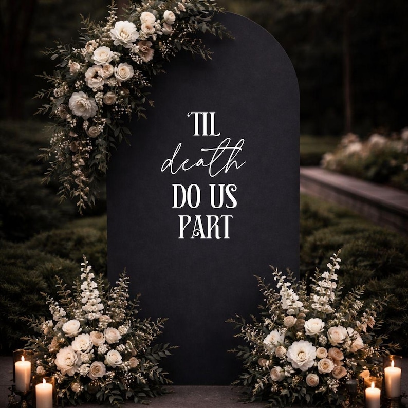 May include: A tall, matte black arched sign featuring the white text 'TIL death DO US PART'. The sign is decorated with large arrangements of white and cream roses, greenery, and small white flowers, with lit pillar candles placed at the base.