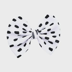 May include: A white bow with a black polka dot pattern. The bow is tied in the center with a matching fabric. The bow is a hair accessory.