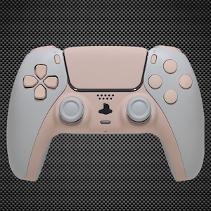 Puede incluir: Un mando inalámbrico PlayStation 5 DualSense rosa y blanco. El mando tiene una placa frontal rosa claro y mangos blancos.