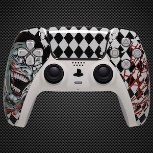 Könnte beinhalten: Ein weißer, individueller PlayStation 5-Controller mit einem Joker-Themen-Design. Die linke Seite zeigt eine detaillierte Illustration des Gesichts des Jokers, während die rechte Seite ein abstraktes rotes und weißes Muster aufweist. Die Oberseite hat ein schwarz-weißes Rautenmuster.