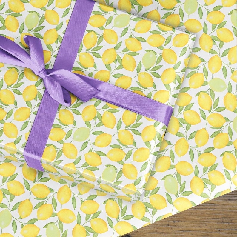 May include: White gift wrap with a repeating pattern of yellow lemons and green leaves. A purple ribbon is tied in a bow on top of the gift wrap.