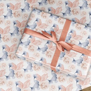 May include: A white gift wrap with a floral pattern in shades of pink and blue. The gift wrap is tied with a peach-colored ribbon.
