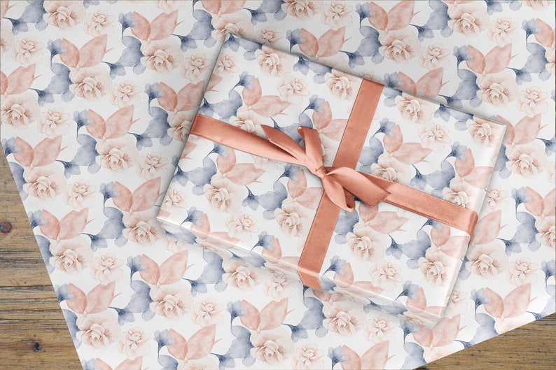 May include: A white gift wrap with a floral pattern in shades of pink and blue. The gift wrap is tied with a peach-colored ribbon.