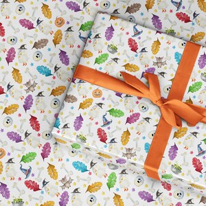 May include: White wrapping paper with a Halloween theme. The paper features a repeating pattern of bats, ghosts, pumpkins, bones, and leaves in shades of orange, green, purple, and blue. A bright orange ribbon is tied around the paper.