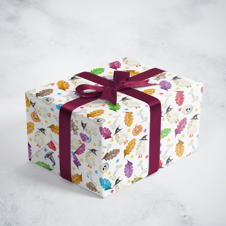 May include: A white gift box with a Halloween-themed wrapping paper. The paper features a pattern of ghosts, pumpkins, bats, and bones in various colors. A burgundy ribbon is tied around the box with a bow.