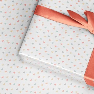 May include: A white gift box with a coral ribbon tied in a bow. The box is wrapped in paper with a pattern of small, colorful hearts.