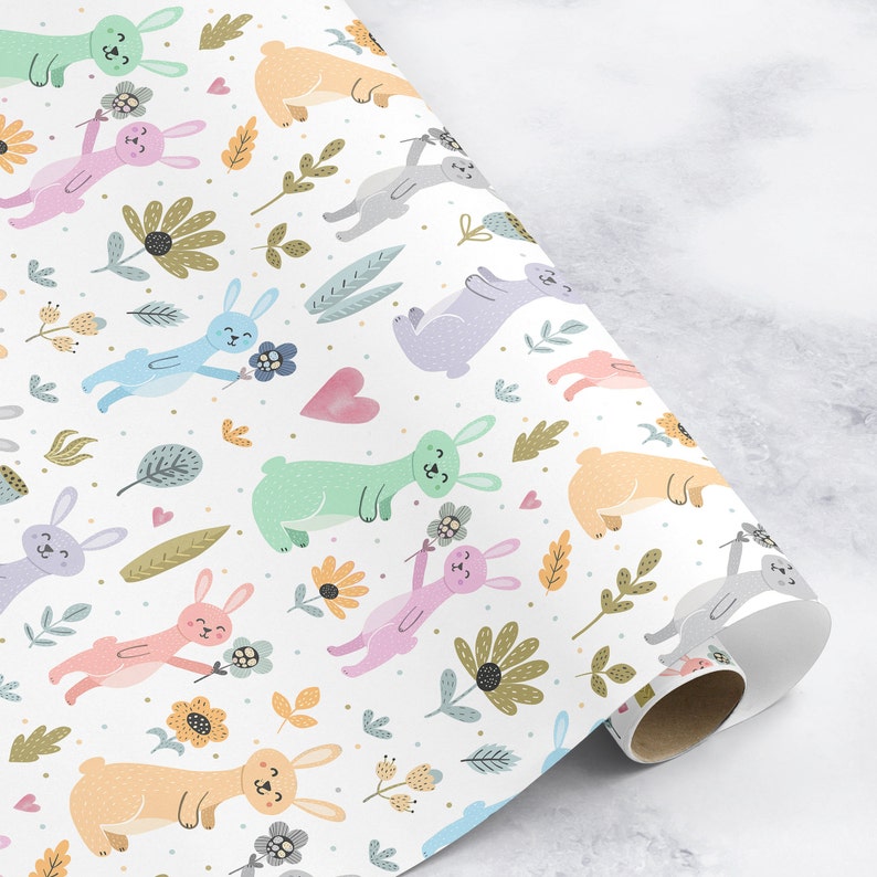 May include: White wrapping paper with a repeating pattern of pastel colored bunnies holding flowers. The bunnies are surrounded by green leaves and small flowers.