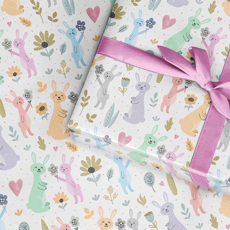 May include: White wrapping paper with a repeating pattern of pastel colored bunnies holding flowers. The bunnies are surrounded by small pink hearts, green leaves, and yellow flowers.