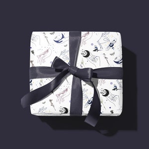 May include: A white gift box with a black ribbon. The box is wrapped in paper with a repeating pattern of hands, moons, stars, and birds.