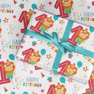 May include: White wrapping paper with a repeating pattern of a red number one, a cartoon lion wearing a party hat, stars, balloons, and the text "Happy Birthday".