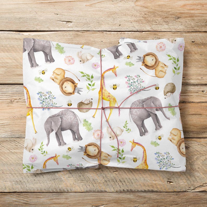 Pode incluir: Uma folha de papel de embrulho branca com um padr&atilde;o repetitivo em aguarela de elefantes cinzentos, girafas amarelas, le&otilde;es castanhos, coelhos pequenos, ouri&ccedil;os, abelhas, flores cor-de-rosa e folhas verdes, atada com um fio vermelho.