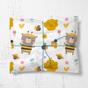 May include: White gift wrap with a bee and honeycomb pattern. The pattern includes yellow honeycombs, bees, and bears wearing bee costumes. The wrap is tied with a blue ribbon.