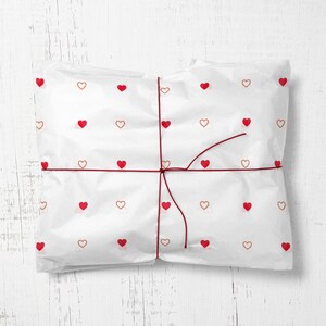 May include: White gift wrapping paper with a red string tied around it. The paper is decorated with a repeating pattern of small red and brown hearts.