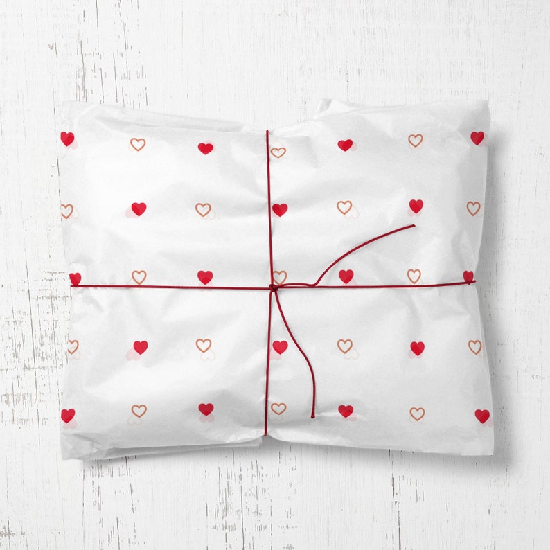 May include: White gift wrapping paper with a red string tied around it. The paper is decorated with a repeating pattern of small red and brown hearts.