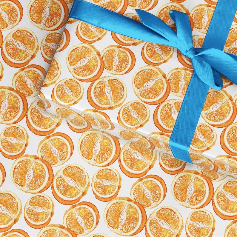 May include: White wrapping paper with a repeating pattern of orange slices. A blue ribbon is tied in a bow on top of the paper.