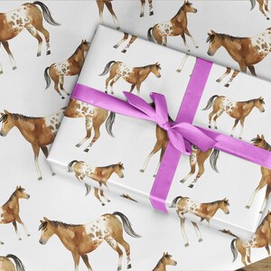 May include: A white gift wrap with a pink ribbon and a repeating pattern of brown and white spotted horses.