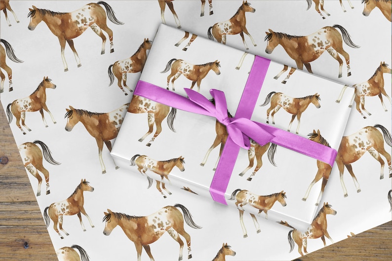 May include: A white gift wrap with a pink ribbon and a repeating pattern of brown and white spotted horses.