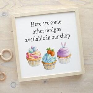 May include: A white sign with a wooden frame and the text "Here are some other designs available in our shop". Three watercolor cupcakes are pictured below the text. One cupcake is decorated with a bunny peeking out of the top, another with pastel pink and blue frosting and sprinkles, and the last with blue frosting and green leaves.